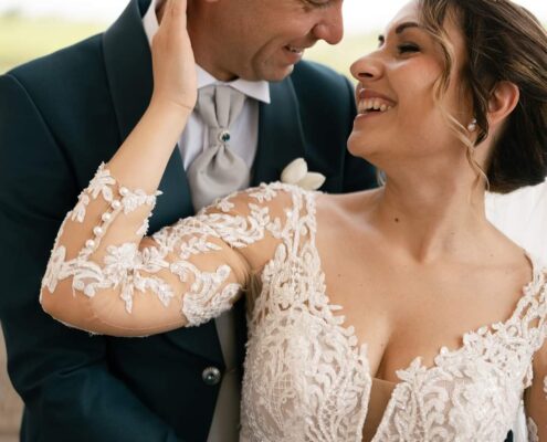 Coppia di sposi sorridenti: lui in abito elegante e lei in abito da sposa raffinato, simbolo di felicità e amore