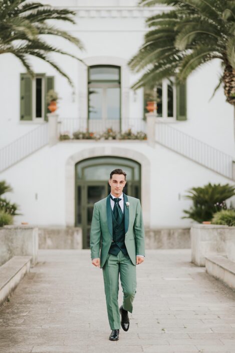 Sposo in abito verde salvia che cammina verso la chiesa, con espressione determinata e felice.