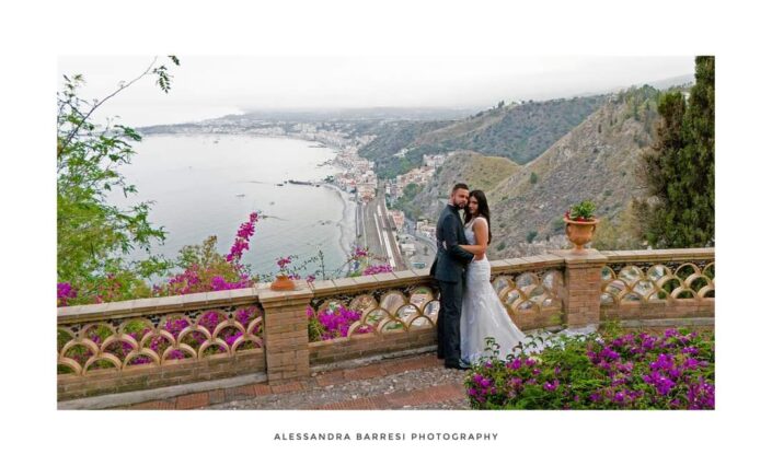 Coppia di sposi abbracciati di fronte a una veduta panoramica del mare, sorridendo felici.