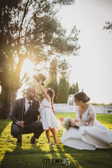 Coppia di sposi felici con la loro bambina che toglie il cappello al papà, sorridendo insieme