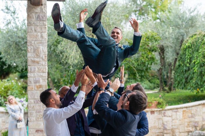 Sposo sollevato in aria dai suoi amici, sorridente e felice durante i festeggiamenti.