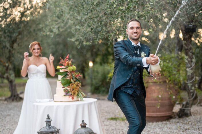 Sposo che stappa una bottiglia di spumante il giorno del matrimonio, sorridendo con gioia.